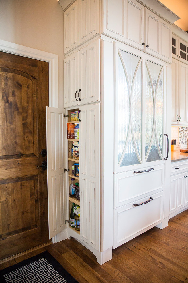 Bild på ett stort flerfärgad flerfärgat kök, med en undermonterad diskho, luckor med upphöjd panel, vita skåp, granitbänkskiva, vitt stänkskydd, stänkskydd i travertin, rostfria vitvaror, mellanmörkt trägolv, en köksö och brunt golv