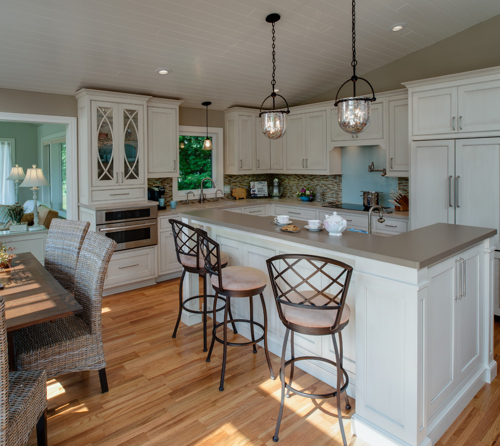 Eat-in kitchen - mid-sized traditional l-shaped medium tone wood floor eat-in kitchen idea in Other with an integrated sink, recessed-panel cabinets, gray cabinets, solid surface countertops, multicolored backsplash, glass sheet backsplash, stainless steel appliances and an island