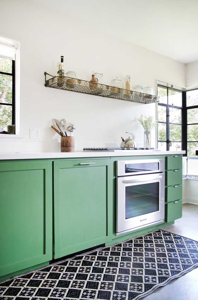 Mid-sized trendy l-shaped concrete floor eat-in kitchen photo in Austin with recessed-panel cabinets, green cabinets, solid surface countertops, white backsplash, stainless steel appliances and an island