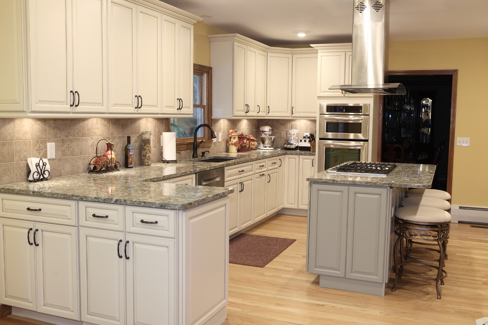 Inspiration for a large transitional u-shaped light wood floor eat-in kitchen remodel in Providence with an undermount sink, raised-panel cabinets, white cabinets, granite countertops, gray backsplash, ceramic backsplash, stainless steel appliances and an island