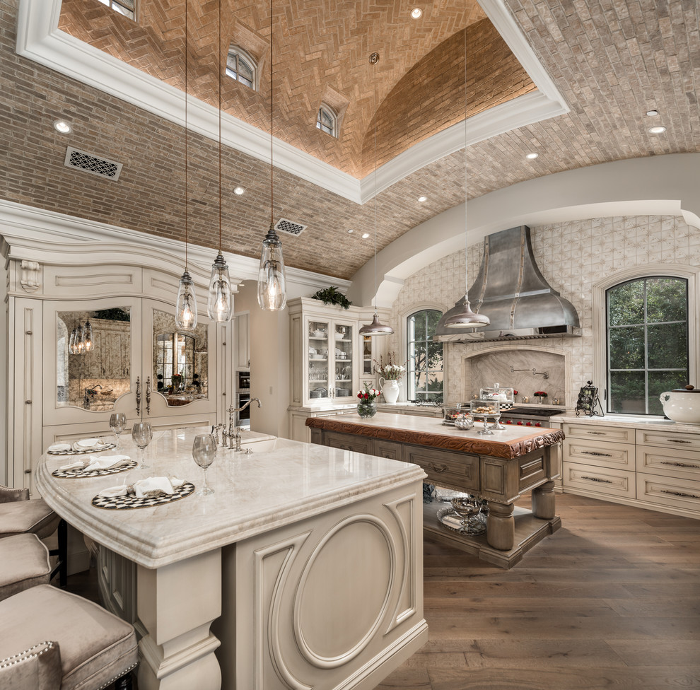 Huge cottage chic u-shaped dark wood floor and brown floor enclosed kitchen photo in Phoenix with a farmhouse sink, raised-panel cabinets, light wood cabinets, quartzite countertops, multicolored backsplash, porcelain backsplash, stainless steel appliances, two islands and beige countertops