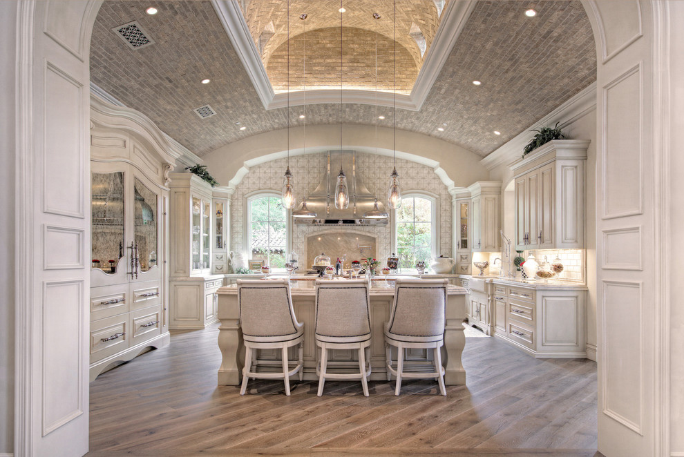 Inspiration for a huge shabby-chic style u-shaped medium tone wood floor, brown floor and tray ceiling enclosed kitchen remodel in Phoenix with a farmhouse sink, recessed-panel cabinets, light wood cabinets, quartzite countertops, multicolored backsplash, marble backsplash, stainless steel appliances, two islands and multicolored countertops
