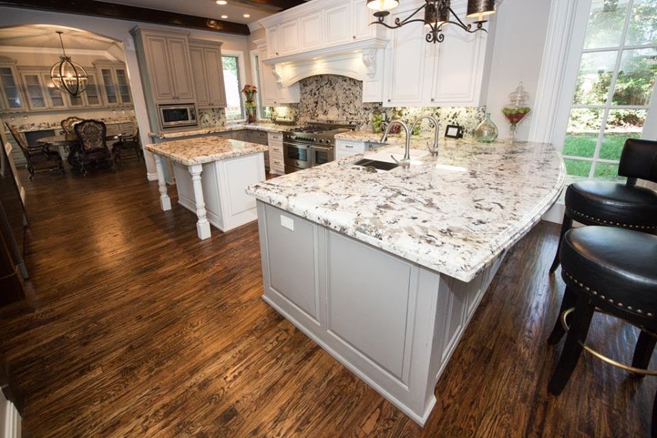 Inspiration for a mid-sized timeless u-shaped dark wood floor and brown floor open concept kitchen remodel in Other with a triple-bowl sink, raised-panel cabinets, white cabinets, granite countertops, multicolored backsplash, stone slab backsplash, stainless steel appliances and an island