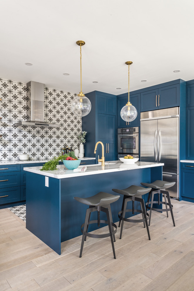 Cette photo montre une cuisine chic avec un placard à porte shaker, des portes de placard bleues, une crédence multicolore, un électroménager en acier inoxydable, parquet clair, îlot, un sol beige et un plan de travail blanc.