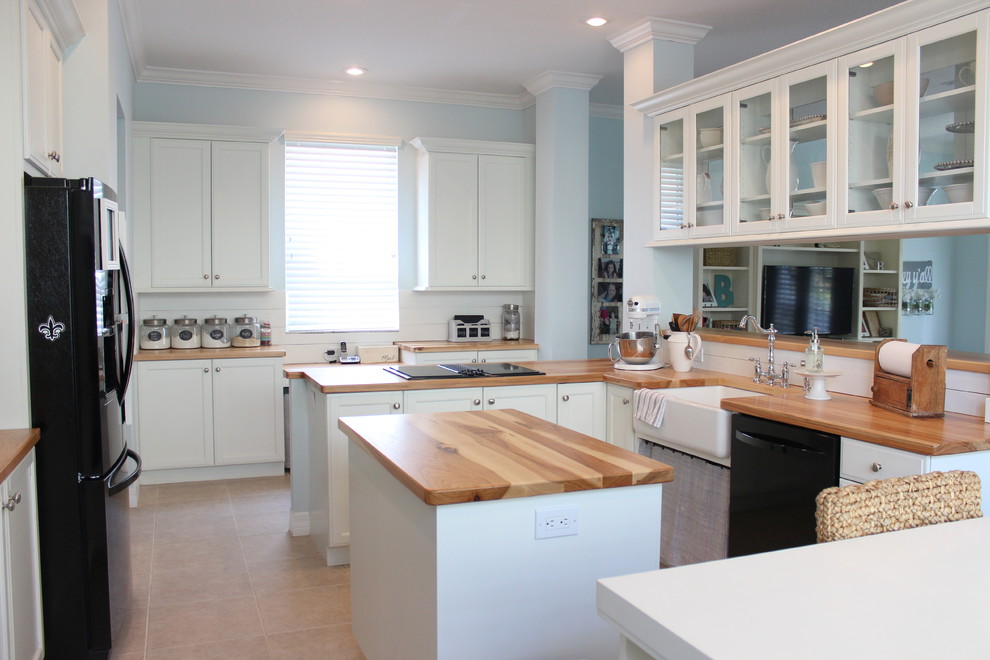 This is an example of a large farmhouse u-shaped open plan kitchen in Tampa with a belfast sink, shaker cabinets, white cabinets, wood worktops, white splashback, porcelain splashback, black appliances, ceramic flooring and an island.