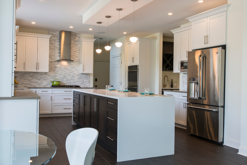 Expansive contemporary l-shaped open plan kitchen in Bridgeport with a submerged sink, shaker cabinets, white cabinets, engineered stone countertops, white splashback, mosaic tiled splashback, stainless steel appliances, porcelain flooring and an island.