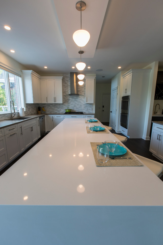 Expansive contemporary l-shaped open plan kitchen in Bridgeport with a submerged sink, shaker cabinets, white cabinets, engineered stone countertops, white splashback, mosaic tiled splashback, stainless steel appliances, porcelain flooring and an island.