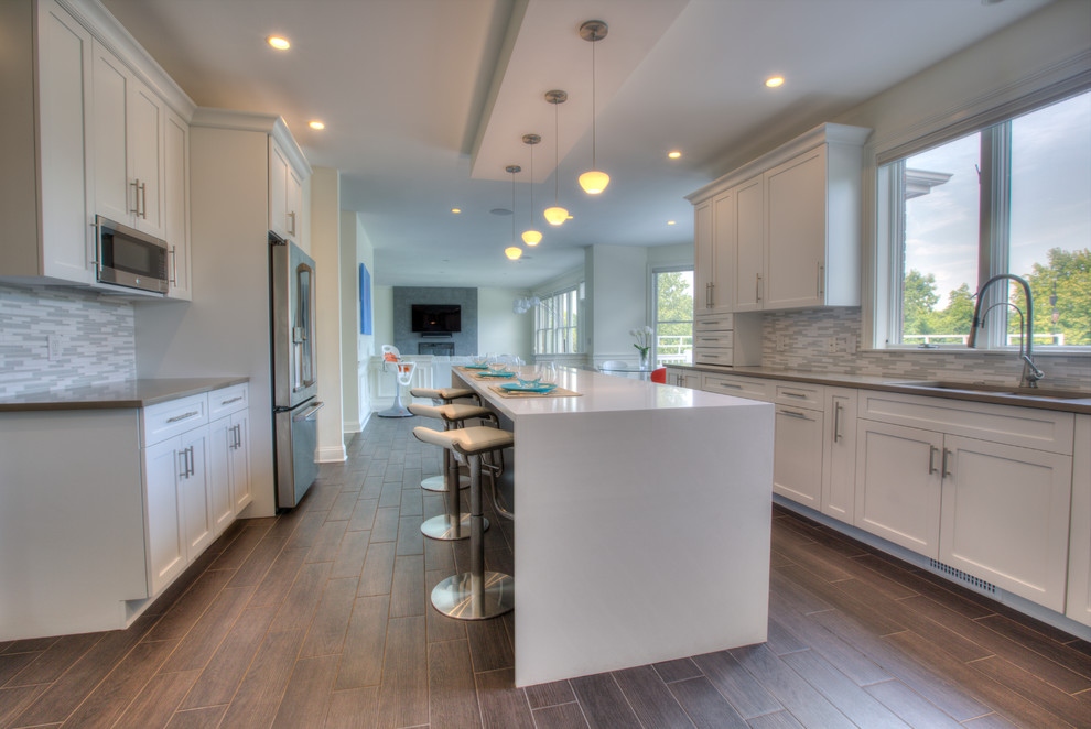 Photo of an expansive contemporary l-shaped open plan kitchen in Bridgeport with a submerged sink, shaker cabinets, white cabinets, engineered stone countertops, white splashback, mosaic tiled splashback, stainless steel appliances, porcelain flooring and an island.