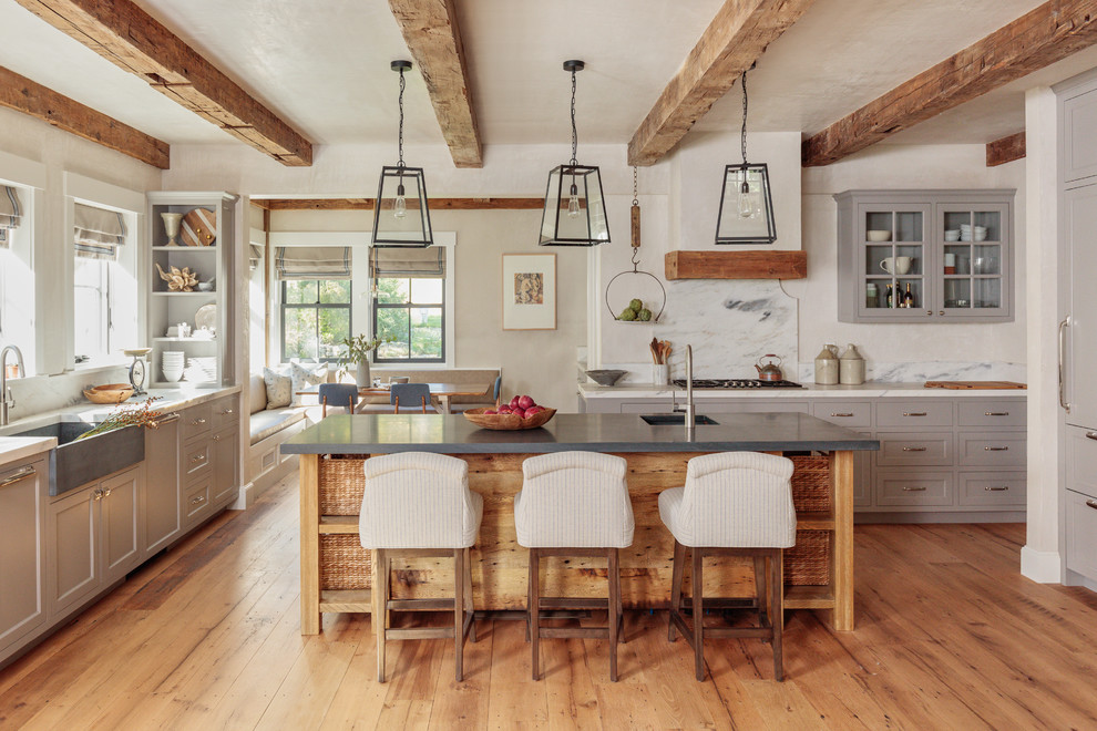 Photo of a rural u-shaped kitchen in Boston with a belfast sink, shaker cabinets, grey cabinets, white splashback, stone slab splashback, integrated appliances, medium hardwood flooring, an island, brown floors and white worktops.