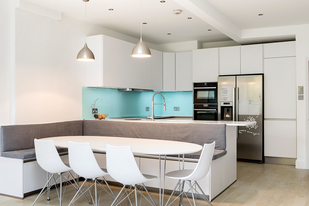 Small contemporary u-shaped open plan kitchen in London with blue splashback, no island, a single-bowl sink, flat-panel cabinets, white cabinets, quartz worktops, glass sheet splashback and stainless steel appliances.