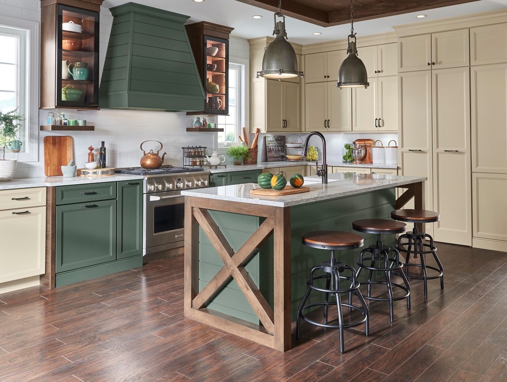 Example of a large country l-shaped dark wood floor and brown floor kitchen design in Minneapolis with an island, a farmhouse sink, recessed-panel cabinets, green cabinets, white backsplash, subway tile backsplash, stainless steel appliances and white countertops