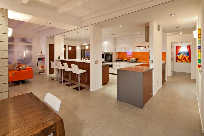 Example of a large trendy u-shaped concrete floor open concept kitchen design in Los Angeles with flat-panel cabinets, white cabinets, stainless steel appliances, an island and orange backsplash
