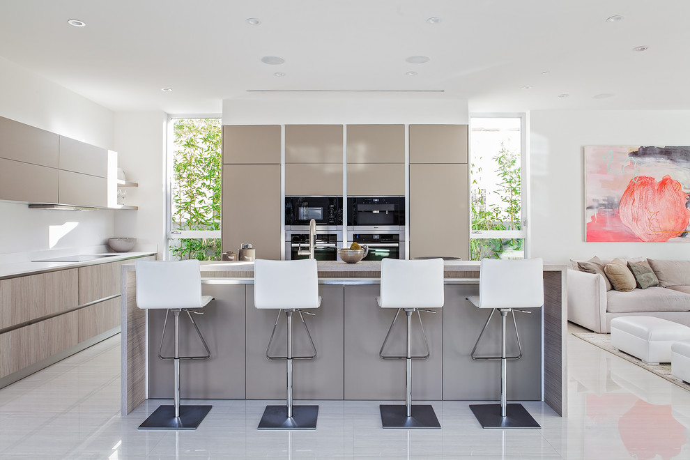 This is an example of a small modern l-shaped open plan kitchen in Los Angeles with flat-panel cabinets, beige cabinets, engineered stone countertops, white splashback, stainless steel appliances, porcelain flooring and an island.