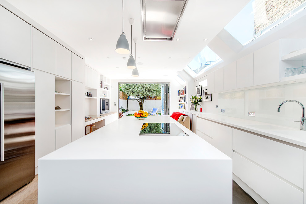 Zweizeilige Moderne Küche mit integriertem Waschbecken, flächenbündigen Schrankfronten, weißen Schränken, Küchenrückwand in Weiß, Glasrückwand, Küchengeräten aus Edelstahl, hellem Holzboden, Kücheninsel und beigem Boden in London