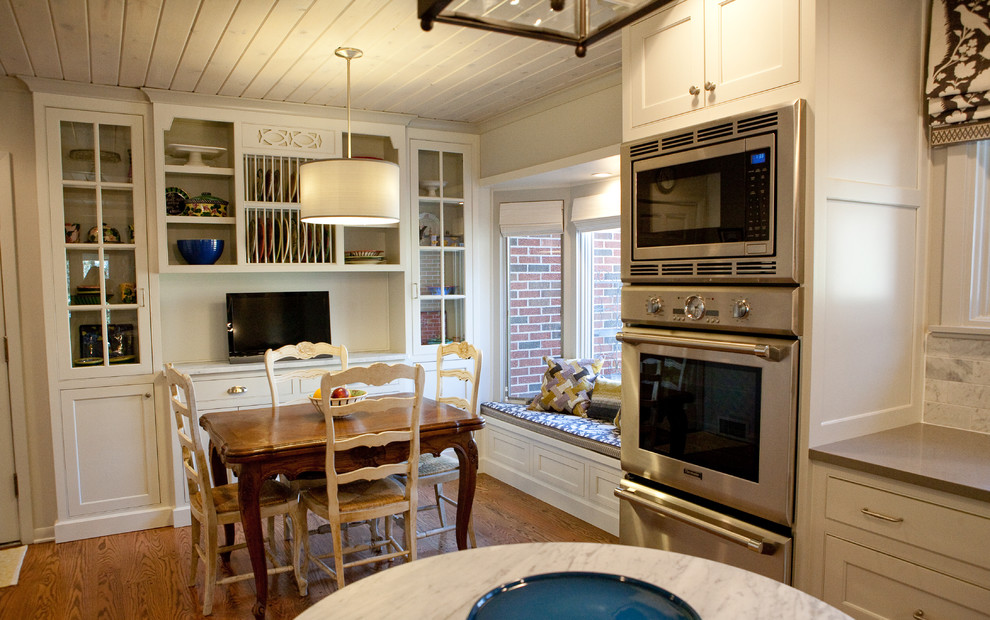 Ejemplo de cocina comedor tradicional con armarios tipo vitrina, puertas de armario blancas, salpicadero blanco, salpicadero de azulejos de piedra, electrodomésticos de acero inoxidable y cortinas