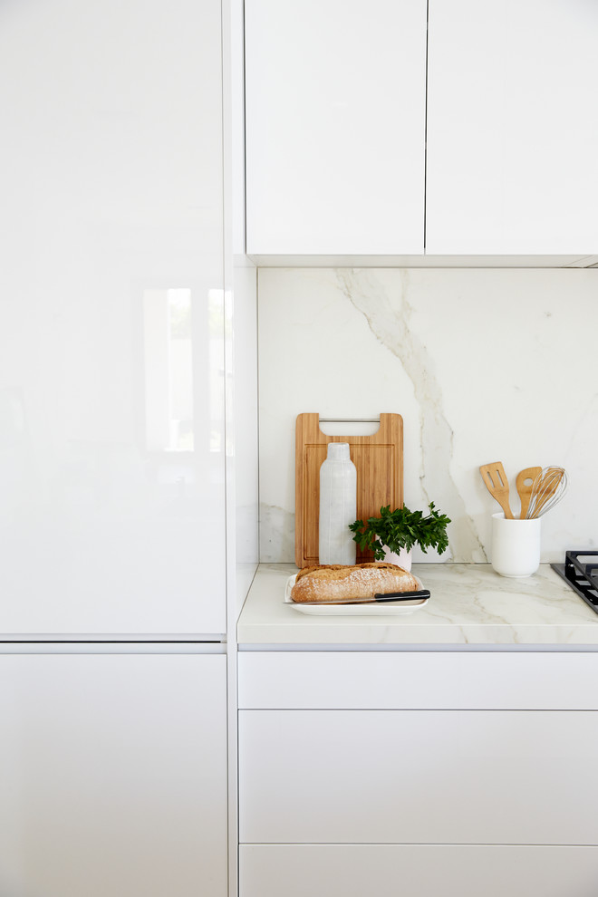 Diseño de cocina moderna con despensa, puertas de armario blancas, encimera de mármol, salpicadero blanco, salpicadero de losas de piedra y una isla