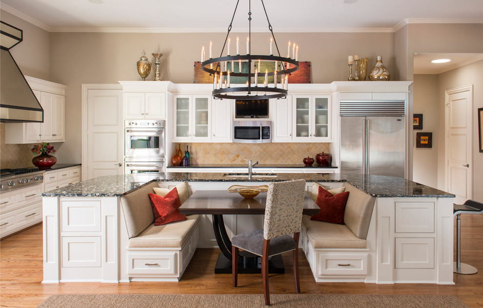 Klassisk inredning av ett stort kök och matrum, med vita skåp, beige stänkskydd, rostfria vitvaror, ljust trägolv och en köksö