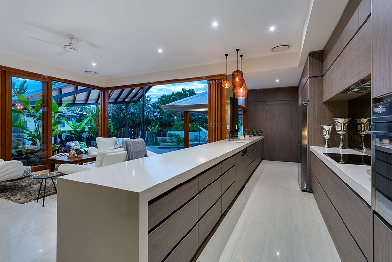 Large world-inspired galley kitchen/diner in Cairns with a submerged sink, engineered stone countertops, metallic splashback, glass sheet splashback, stainless steel appliances, porcelain flooring and an island.