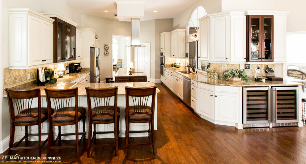 Example of a huge classic u-shaped medium tone wood floor eat-in kitchen design in Orlando with an undermount sink, raised-panel cabinets, white cabinets, granite countertops, beige backsplash, stone tile backsplash and an island