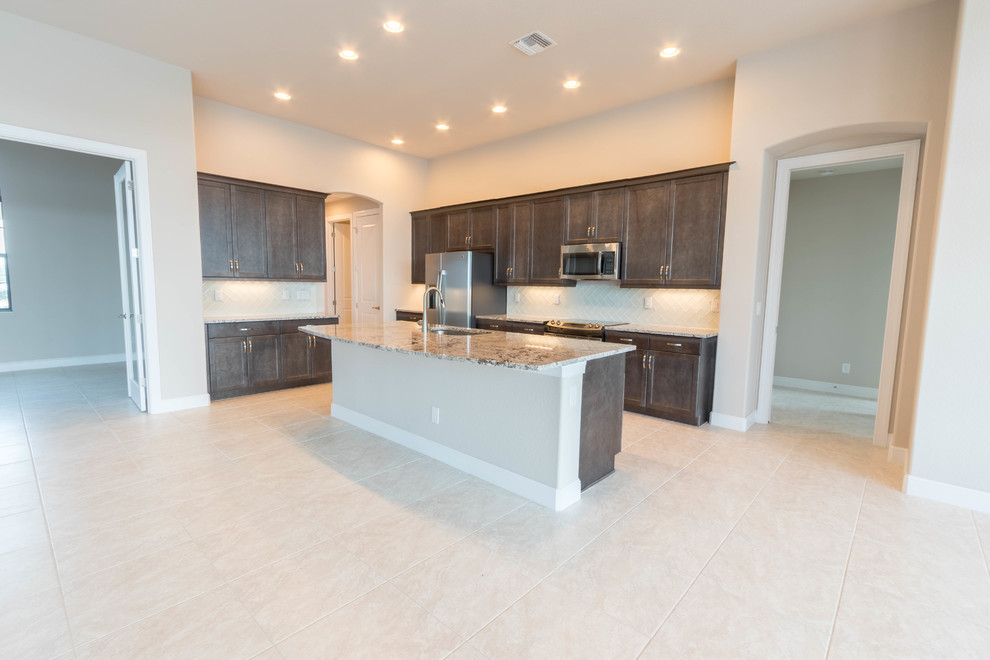 This is an example of a medium sized classic l-shaped open plan kitchen in Miami with a double-bowl sink, shaker cabinets, brown cabinets, granite worktops, white splashback, glass tiled splashback, stainless steel appliances, ceramic flooring, an island and beige floors.