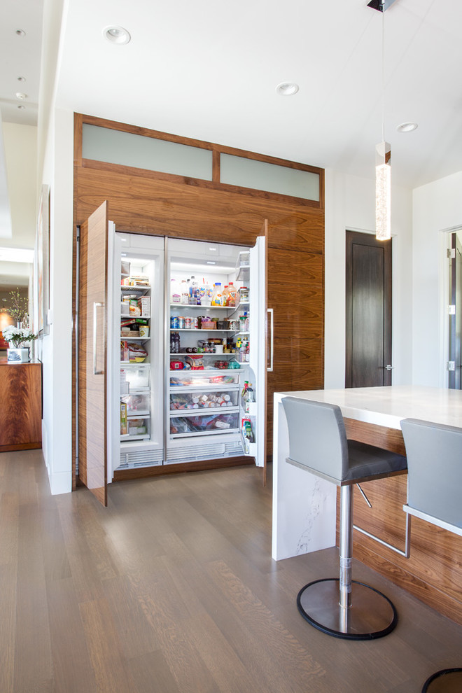 Inspiration for a medium sized contemporary u-shaped kitchen pantry in Salt Lake City with a built-in sink, flat-panel cabinets, brown cabinets, quartz worktops, white splashback, metro tiled splashback, stainless steel appliances, light hardwood flooring, an island, grey floors and white worktops.