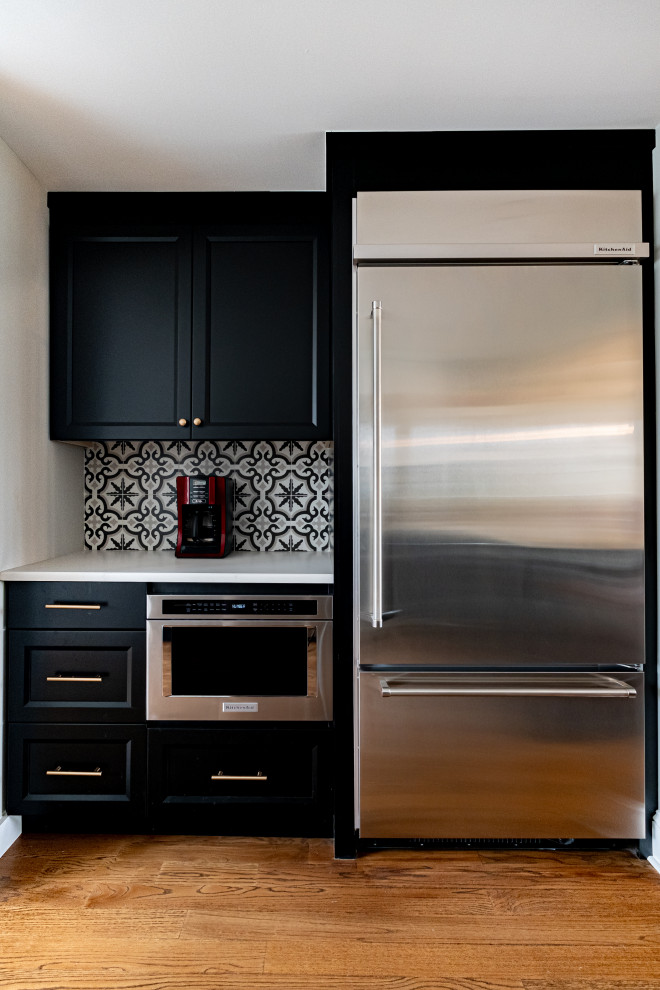 Klassisk inredning av ett mellanstort vit vitt kök, med en undermonterad diskho, svarta skåp, bänkskiva i kvartsit, flerfärgad stänkskydd, stänkskydd i porslinskakel, rostfria vitvaror, mellanmörkt trägolv, en halv köksö och skåp i shakerstil