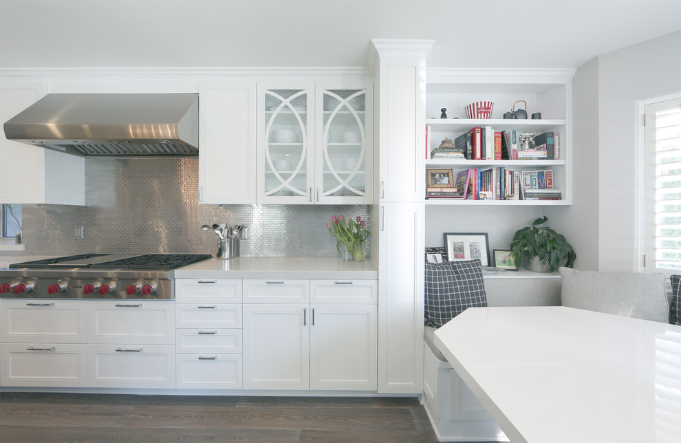 Exempel på ett klassiskt kök, med en undermonterad diskho, luckor med infälld panel, vita skåp, bänkskiva i kvarts, grått stänkskydd, stänkskydd i metallkakel, rostfria vitvaror, mellanmörkt trägolv och en köksö