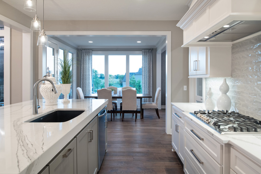 Inspiration for a craftsman galley medium tone wood floor and brown floor open concept kitchen remodel in Kansas City with a drop-in sink, white cabinets, white backsplash, stainless steel appliances, an island and white countertops
