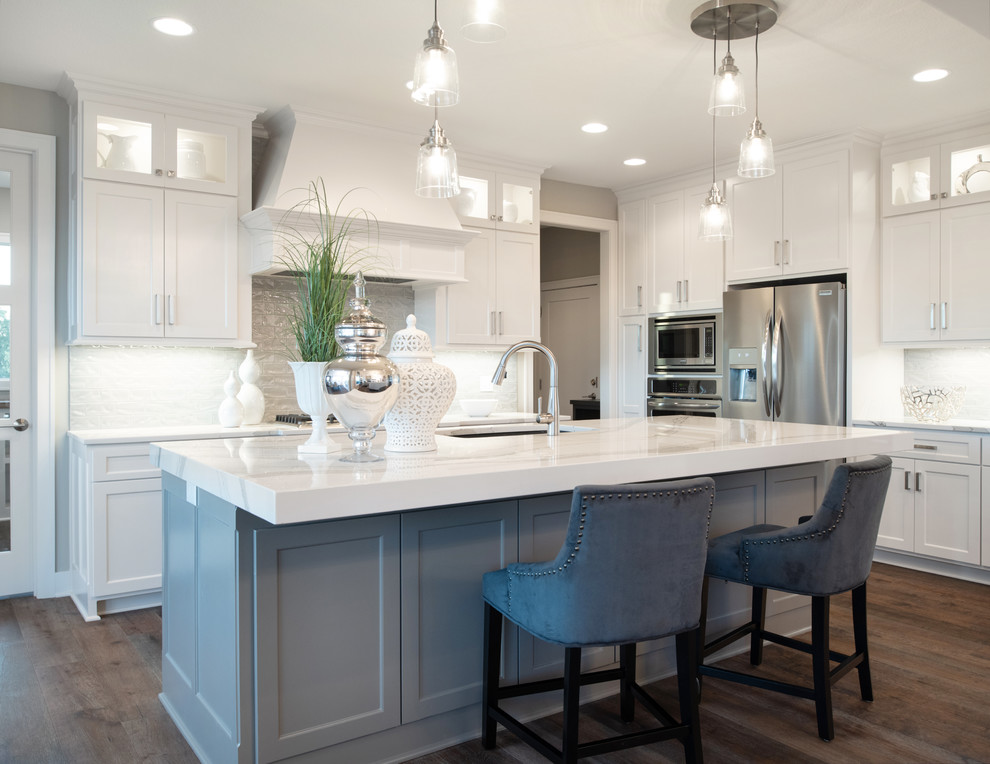 Traditional galley open plan kitchen in Kansas City with a built-in sink, white cabinets, white splashback, stainless steel appliances, medium hardwood flooring, an island, brown floors and white worktops.