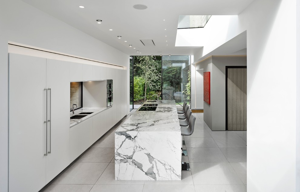Modern inredning av ett kök, med en undermonterad diskho, släta luckor, vita skåp, marmorbänkskiva, integrerade vitvaror, en köksö och vitt golv