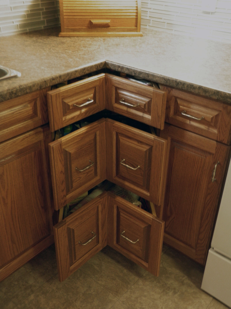 Exempel på ett avskilt, litet klassiskt l-kök, med en dubbel diskho, luckor med upphöjd panel, skåp i mellenmörkt trä, laminatbänkskiva, grått stänkskydd, glaspanel som stänkskydd, vita vitvaror och vinylgolv