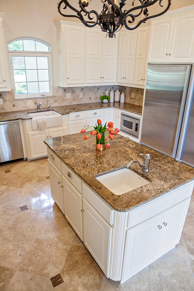 Kitchen - large traditional travertine floor kitchen idea in Other with a farmhouse sink, recessed-panel cabinets, white cabinets, granite countertops, travertine backsplash, stainless steel appliances and an island