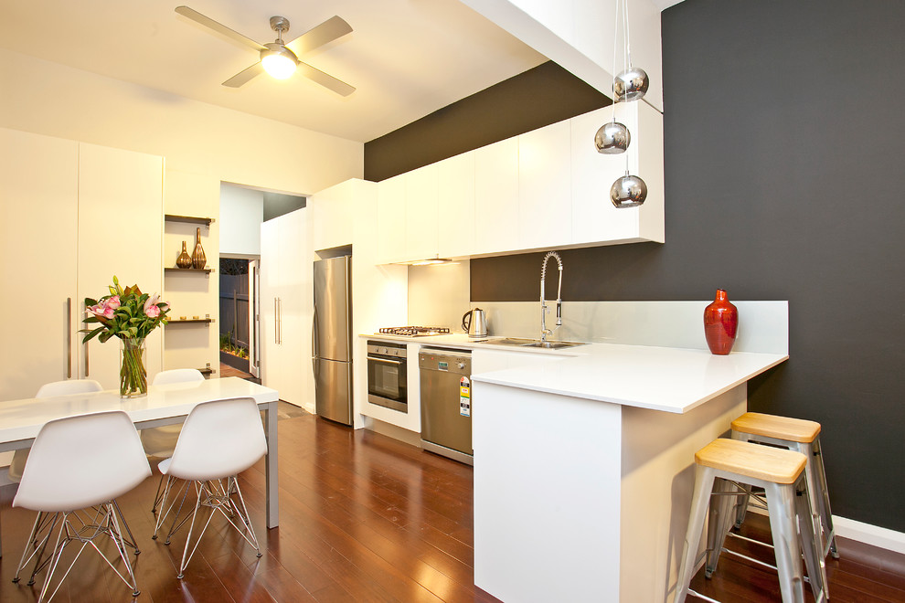 Moderne Wohnküche mit Doppelwaschbecken, flächenbündigen Schrankfronten, weißen Schränken, Küchenrückwand in Weiß, Küchengeräten aus Edelstahl und braunem Holzboden in Sydney