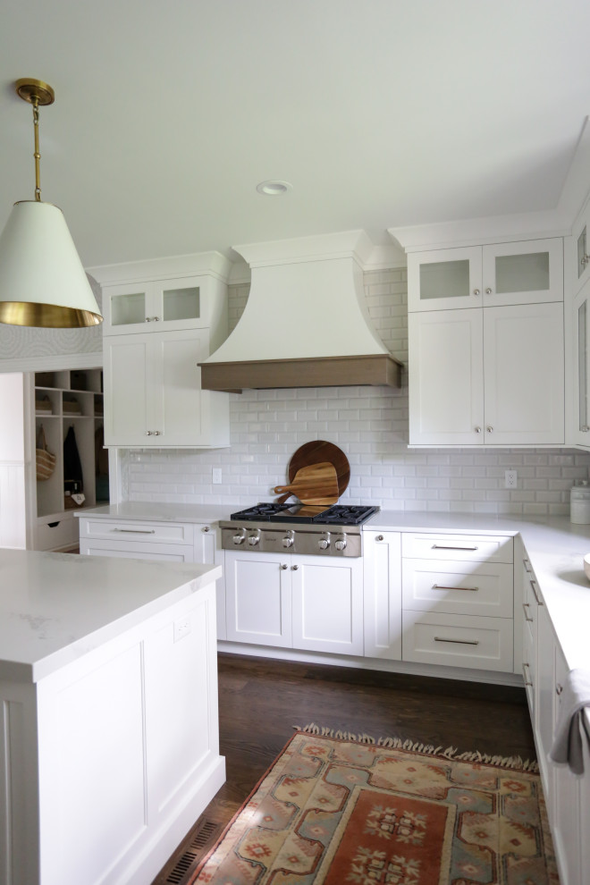 Large classic u-shaped kitchen/diner in Indianapolis with a belfast sink, recessed-panel cabinets, white cabinets, engineered stone countertops, white splashback, metro tiled splashback, integrated appliances, medium hardwood flooring, an island, brown floors and white worktops.