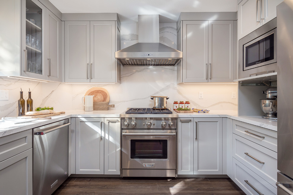 Foto på ett mellanstort funkis vit kök och matrum, med en undermonterad diskho, vita skåp, bänkskiva i kvarts, vitt stänkskydd, stänkskydd i glaskakel, rostfria vitvaror, mellanmörkt trägolv och brunt golv