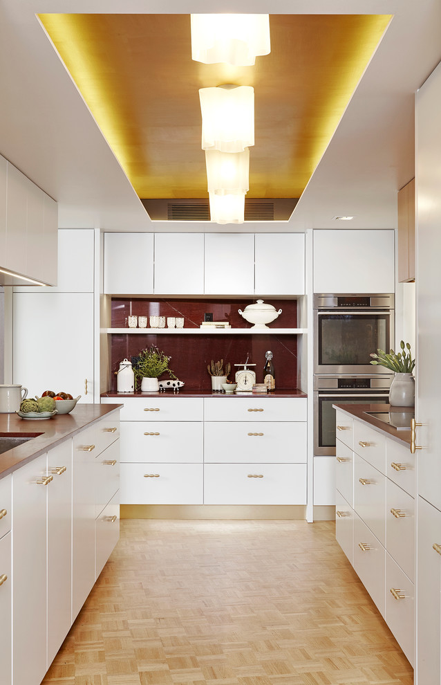 Modern inredning av ett avskilt, litet u-kök, med en undermonterad diskho, släta luckor, vita skåp, marmorbänkskiva, rött stänkskydd, stänkskydd i sten, rostfria vitvaror och ljust trägolv