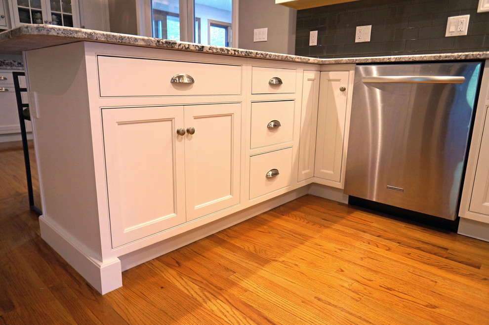 Inspiration for a mid-sized timeless u-shaped medium tone wood floor eat-in kitchen remodel in Boston with an undermount sink, beaded inset cabinets, white cabinets, granite countertops, gray backsplash, glass tile backsplash, stainless steel appliances and a peninsula