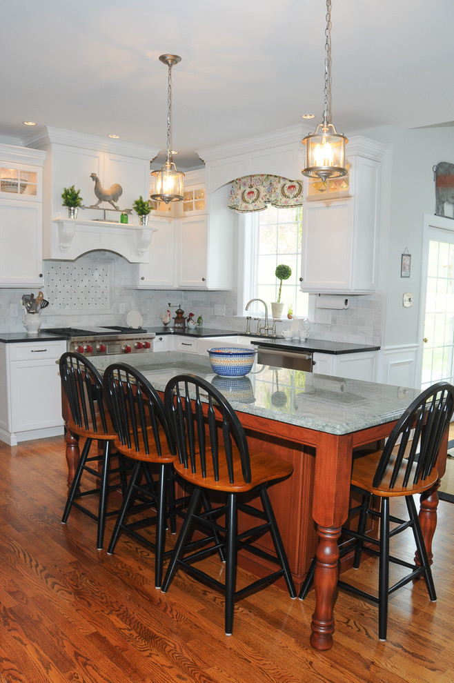 Bild på ett mellanstort lantligt kök, med en rustik diskho, luckor med upphöjd panel, vita skåp, granitbänkskiva, grått stänkskydd, stänkskydd i tunnelbanekakel, rostfria vitvaror, mellanmörkt trägolv, en köksö och brunt golv