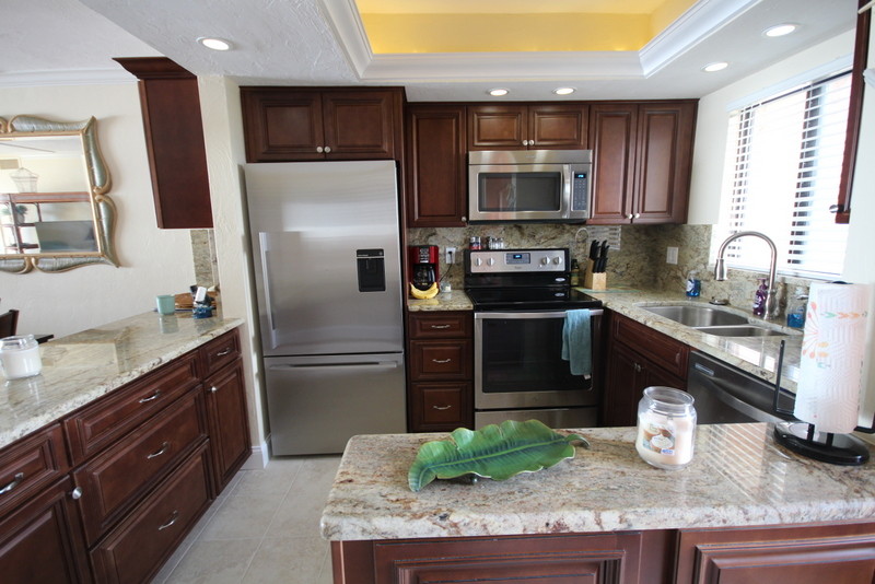 Bild på ett mellanstort tropiskt kök, med en undermonterad diskho, luckor med upphöjd panel, skåp i mellenmörkt trä, granitbänkskiva, beige stänkskydd, stänkskydd i sten, rostfria vitvaror och klinkergolv i porslin