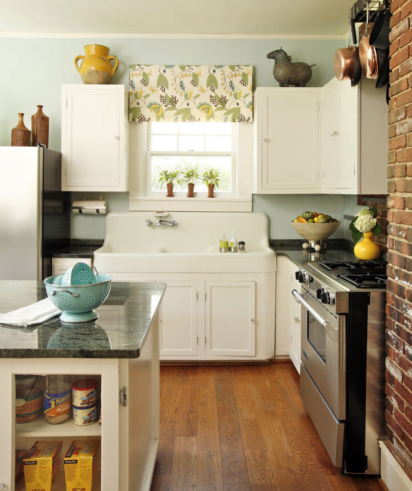 Inspiration for a mid-sized eclectic l-shaped medium tone wood floor kitchen remodel in Dallas with a farmhouse sink, recessed-panel cabinets, white cabinets, granite countertops, stainless steel appliances, black backsplash and an island