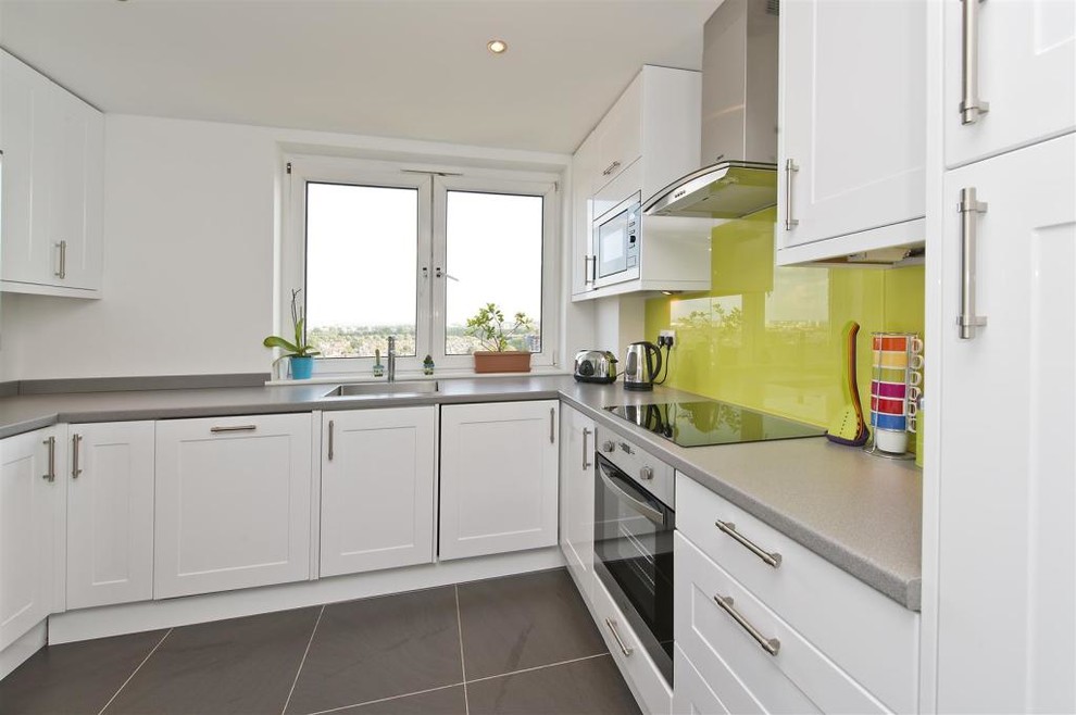 Medium sized contemporary u-shaped kitchen pantry in London with a submerged sink, shaker cabinets, yellow cabinets, laminate countertops, green splashback, glass sheet splashback, stainless steel appliances, porcelain flooring and no island.