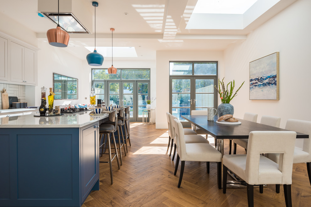 Classic kitchen/diner in London with shaker cabinets, blue cabinets, white splashback, medium hardwood flooring, an island, brown floors and white worktops.