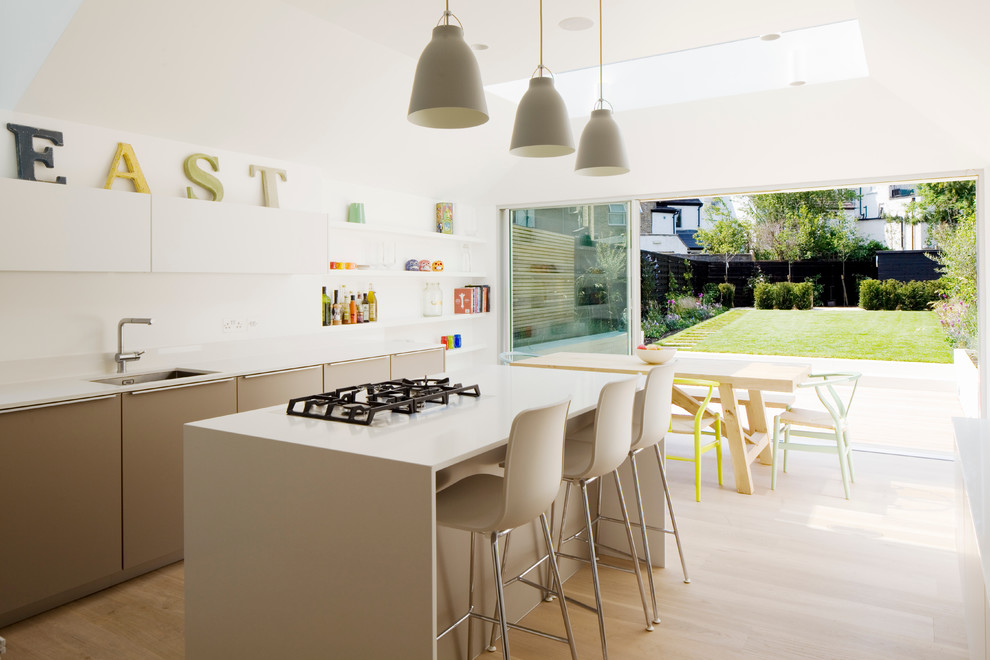 Inspiration for a mid-sized contemporary l-shaped light wood floor and beige floor eat-in kitchen remodel in London with flat-panel cabinets, solid surface countertops, white backsplash, an island, an undermount sink, beige cabinets, glass sheet backsplash, stainless steel appliances and beige countertops
