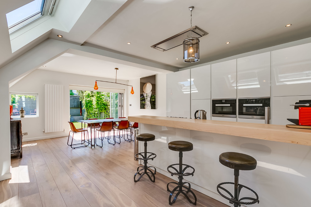 Example of a trendy single-wall dark wood floor open concept kitchen design in London with flat-panel cabinets, white cabinets and an island