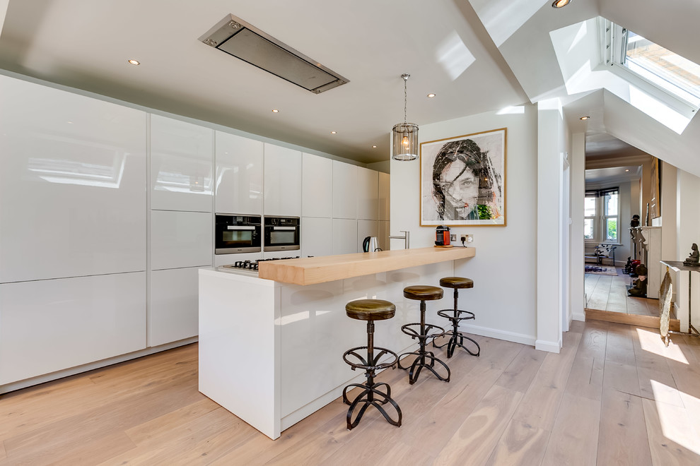Photo of a contemporary galley open plan kitchen in London with flat-panel cabinets, white cabinets, dark hardwood flooring, an island, white appliances and white worktops.