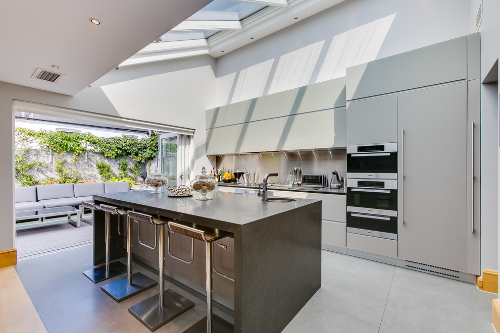 Medium sized contemporary single-wall enclosed kitchen in London with a submerged sink, flat-panel cabinets, grey cabinets, metallic splashback, metal splashback, stainless steel appliances, ceramic flooring, an island, grey floors and grey worktops.