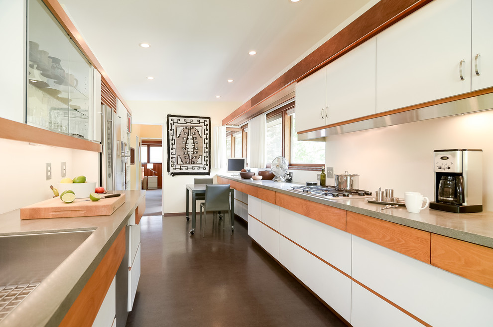 Cette image montre une cuisine parallèle design avec un évier encastré, un placard à porte plane, des portes de placard blanches, une crédence blanche et sol en béton ciré.