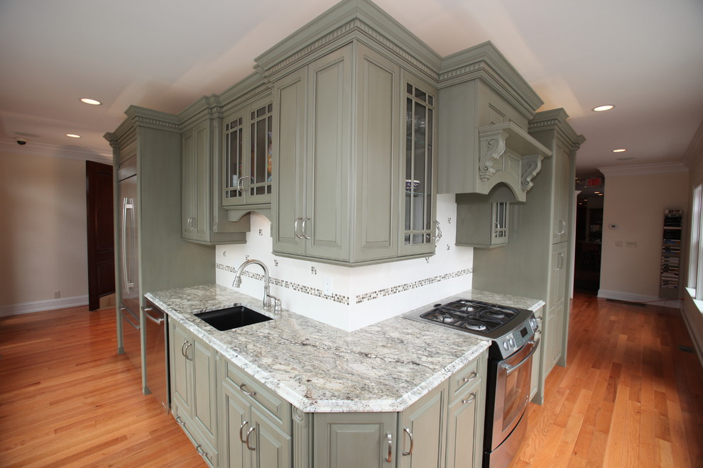 Klassisk inredning av ett flerfärgad flerfärgat kök, med en undermonterad diskho, luckor med upphöjd panel, gröna skåp, granitbänkskiva, flerfärgad stänkskydd, stänkskydd i keramik, rostfria vitvaror, mellanmörkt trägolv och brunt golv