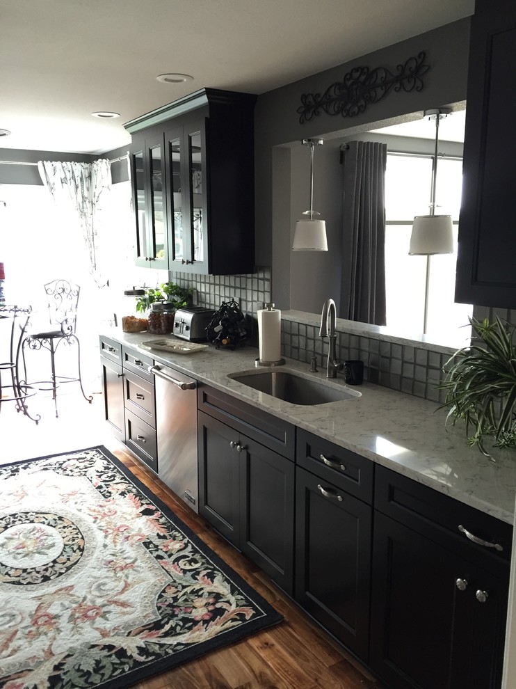 Klassisk inredning av ett litet kök, med en undermonterad diskho, luckor med infälld panel, svarta skåp, marmorbänkskiva, stänkskydd med metallisk yta, stänkskydd i metallkakel, rostfria vitvaror, mellanmörkt trägolv och brunt golv