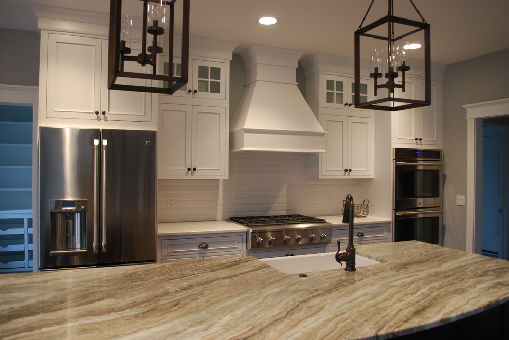 Example of a large trendy medium tone wood floor and brown floor eat-in kitchen design in Cleveland with a farmhouse sink, beaded inset cabinets, white cabinets, granite countertops, white backsplash, subway tile backsplash, stainless steel appliances and an island